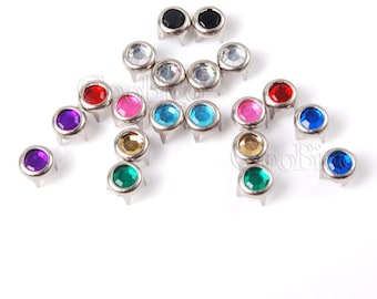 May include: Assortment of colorful round rhinestones with silver settings. The rhinestones are in various colors, including red, blue, green, purple, pink, and clear. The rhinestones are set on a white background.
