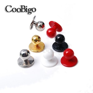 May include: Assortment of seven round, plastic and metal buttons with a flat base and a round top. The buttons are in various colours, including red, white, black, gold and silver.