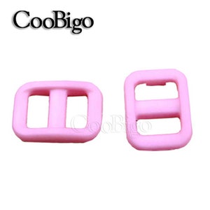 Op de afbeelding: Twee roze plastic schuifgespen. De gespen zijn rechthoekig met een middelste balk en twee gaten aan elke kant.