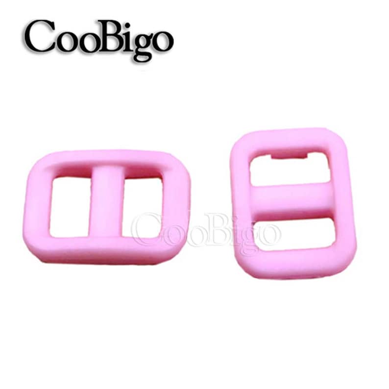 Op de afbeelding: Twee roze plastic schuifgespen. De gespen zijn rechthoekig met een middelste balk en twee gaten aan elke kant.