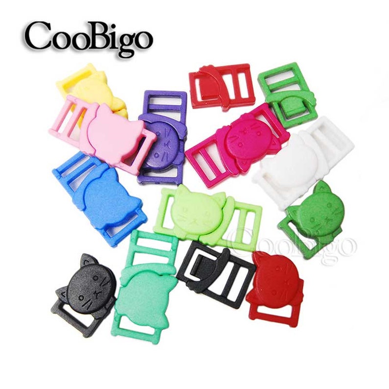 Op de afbeelding: Assortiment van kleurrijke plastic kattenvormige schuifgespen. De gespen zijn in verschillende kleuren, waaronder roze, blauw, groen, rood, zwart, wit en geel. De gespen zijn ontworpen voor gebruik met band of riemen.
