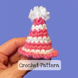 May include: A pink and white crocheted party hat with a white pom-pom on top. The hat is held in a hand and the text "Crochet Pattern" is below the hat.