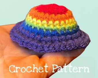 Puede incluir: Un pequeño gorro de crochet arcoíris con un borde morado. El gorro se está sosteniendo en una mano, y el texto "Crochet Pattern" es visible debajo del gorro.