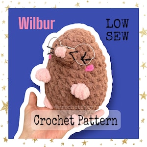 May include: Crochet pattern for a brown mole with pink accents, wearing glasses. The pattern is called "Wilbur" and is described as "Low Sew".