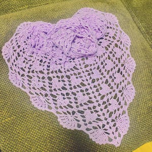 Könnte beinhalten: Eine herzförmige, violette Häkeldeckchen mit komplizierten Blumenmustern. Die Deckchen liegt auf einer grünen Stoffoberfläche.