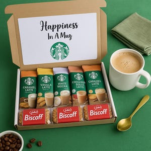May include: A gift box containing Starbucks coffee packets and Biscoff biscuits. The box includes Caramel, Vanilla, White Mocha, Cinnamon Dolce, and Caramel Latte packets. A white mug of coffee and a gold spoon are on a green surface.