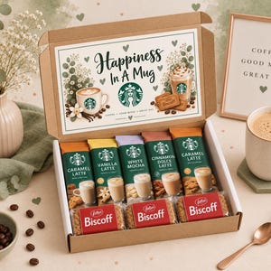 May include: A cardboard gift box containing five Starbucks coffee drink packets labelled Caramel Latte, Vanilla Latte, White Mocha, Cinnamon Dolce Latte, and Caramel Latte, alongside three Lotus Biscoff biscuit packs. The box lid features the text Happiness In A Mug.