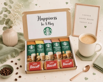 May include: A gift box labelled Happiness In A Mug with a Starbucks logo containing five coffee drink mix packets in Caramel, Vanilla, White Mocha, Cinnamon Dolce, and Caramel flavours, plus three Biscoff biscuit packs, a mug, and a framed sign.