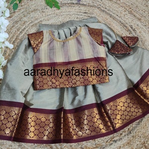 May include: A traditional Indian children's outfit in silver-gray, featuring a skirt and a top. The top has a striped pattern with gold trim and the text "aaradhyafashions". The skirt and top are trimmed with a gold floral design and a deep red border.
