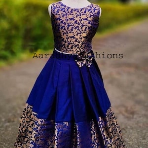 Peut inclure: Une lehenga choli en soie jacquard bleu et or. Le haut sans manches pr&eacute;sente un motif floral dor&eacute; sur fond bleu. La jupe est pliss&eacute;e bleue avec des accents floraux dor&eacute;s. Une ceinture blanche et une fleur ornent l'ensemble.
