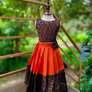 Peut inclure: Robe sans manches sur mannequin. Le corsage est noir avec un motif floral. La jupe est pliss&eacute;e, avec des panneaux orange et noirs. Un n&oelig;ud noir est &agrave; la taille. Le texte "Aaradhyafashions" est visible.