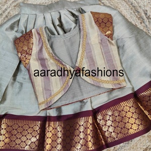 May include: A traditional outfit featuring a silver-gray skirt and a matching top. The vest is striped with gold trim and maroon accents. The skirt has a maroon and gold patterned border. The text "aaradhyafashions" is visible.