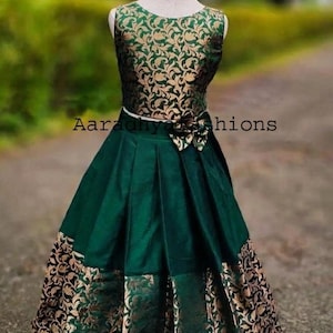 Peut inclure: Une lehenga choli en soie jacquard verte et dor&eacute;e. Le haut sans manches pr&eacute;sente un motif floral dor&eacute; sur fond vert. La jupe est verte avec des panneaux &agrave; motifs floraux dor&eacute;s. Le texte "Aaradhya Fashions" est visible.
