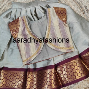 May include: A silver-gray traditional outfit featuring a pleated skirt and a matching top. The outfit includes a striped vest with gold trim and maroon accents. The text "aaradhyafashions" is visible.
