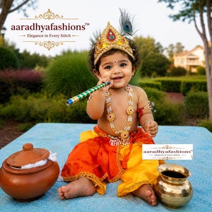 May include: A child dressed as Lord Krishna wearing a gold crown with a peacock feather, a multi-strand pearl necklace with gold accents, and a two-tone orange and yellow dhoti. The child holds a green and gold flute near a clay pot and brass pot.