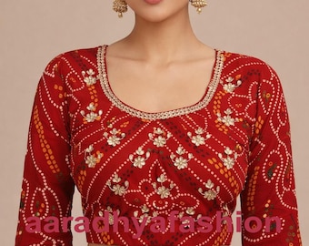 May include: Red blouse with a decorative floral pattern and gold trim. The three-quarter sleeves and neckline are also trimmed with gold. The text "aaradhyafashion" is visible on the blouse.