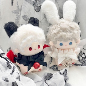 May include: Two plush dolls with bunny ears. One doll has black ears, a black bow, and a red bell. The other doll has white ears and a white outfit. Both dolls have fluffy white hair, red eyes, and a cute design.