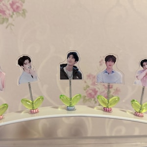 May include: Five decorative photo holders featuring images of people. Each holder has a clear plastic image attached to a silver spring, with a green leaf-shaped base and a pink and blue accent.