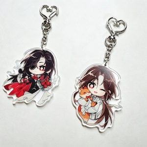 Pode incluir: Dois chaveiros de acrílico com ilustrações em estilo anime. Um apresenta um personagem com uma roupa preta e vermelha segurando flores, o outro mostra um personagem com uma raposa. Ambos têm fechos prateados em forma de coração.
