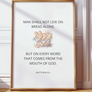Op de afbeelding: Een witte achtergrond met zwarte tekst die luidt: "De mens zal niet van brood alleen leven, maar van elk woord dat uit de mond van God komt. Mattheüs 4:4." Er is een aquarelillustratie van een mand met brood.