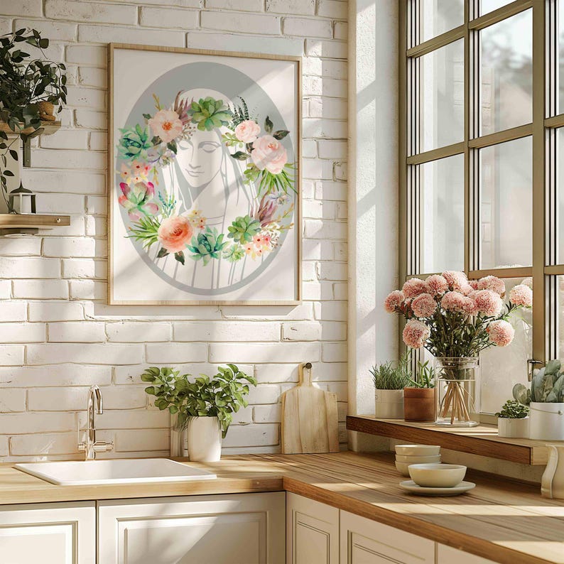 May include: A framed print of a woman's face with a floral wreath around her head. The wreath is made of succulents, flowers, and greenery. The background is a light gray color.