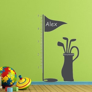 May include: A green wall with a height chart featuring a golf bag and clubs with the name "Alex" and the text "Marshfield" on it. The chart is next to a chalkboard with the numbers 0-9 on it. There are also wooden blocks, a toy truck, and a colorful puzzle ball on the floor.