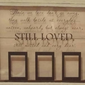 以下が含まれることがあります： 愛と喪失についての引用が書かれたガラス窓付きの白い木製のフレーム。引用は次のとおりです。「私たちが愛する人は去りません。彼らは毎日私たちのそばを歩きます... 見えない、聞こえない、しかし常に近く、いつも愛され、いつも恋しがられ、とても大切です。」フレームには、空の額縁が3つあります。