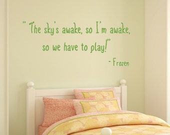 May include: A white wooden bed with a yellow and pink floral bedspread and a green and white striped pillow. The wall behind the bed has a green quote from the movie Frozen that reads "The sky's awake, so I'm awake, so we have to play!" - Frozen.