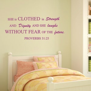 May include: A white bedroom with a white bed, a green rug, and a green bench. The wall has a pink and white quote that reads "SHE is CLOTHED in Strength AND Dignity AND SHE laughs WITHOUT FEAR OF THE future. PROVERBS 31:25"