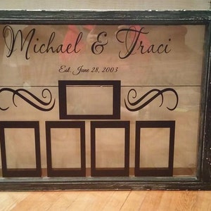 May include: A black framed picture frame with a glass front and a white background. The frame has five openings for pictures, each with a black border. The frame has the text "Michael & Traci Est. June 28, 2003" printed on it.