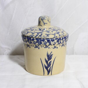 May include: A beige ceramic jar with a lid, featuring a blue floral pattern on the lid and rim. A blue wheat stalk design is painted on the front of the jar. The jar is a classic kitchen storage container.