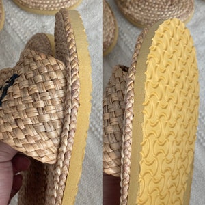May include: Close-up of a pair of woven straw sandals with a yellow rubber sole. The sandals have a braided strap detail around the edge.