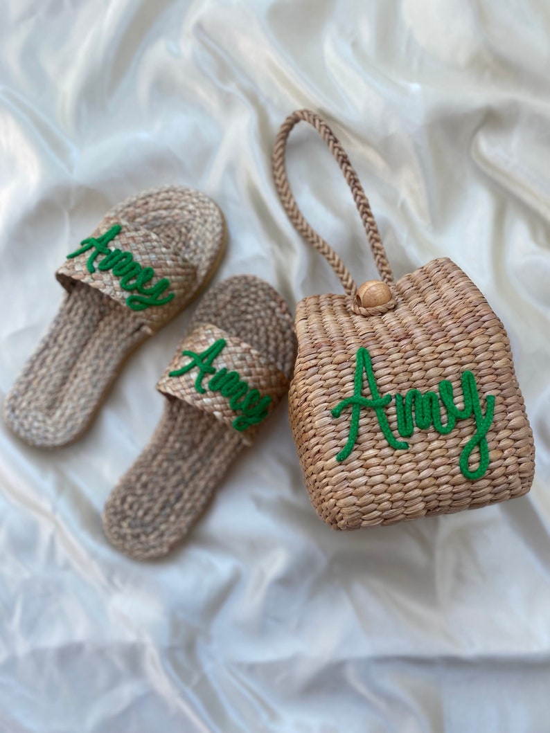May include: Two pairs of woven straw sandals with green embroidered lettering that says "Amy" and a woven straw tote bag with a green embroidered handle and lettering that says "Amy".