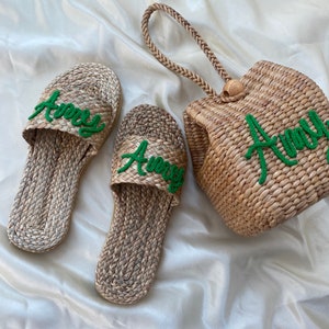 May include: Two pairs of woven straw sandals with green embroidered lettering that says "Awny" and a woven straw tote bag with the same green embroidered lettering.