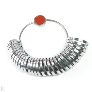 May include: A silver ring sizer with a red knob. The sizer has a series of rings numbered 1 through 15.