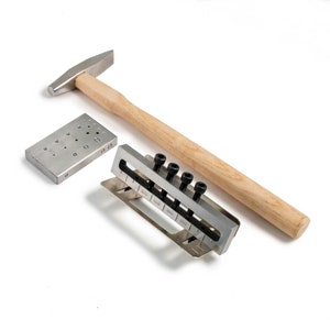 May include: A set of metal tools for leather crafting, including a hammer, a metal plate with holes of different sizes, and a metal plate with a row of metal posts. The metal posts are labeled with different sizes: 3/32, 1/8, 5/32, 3/16, 7/32, and 1/4.