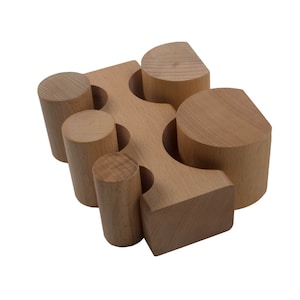 Puede incluir: Un conjunto de bloques de madera de diferentes formas, incluyendo cilindros, semicírculos y una base rectangular. Los bloques son de madera marrón claro y están dispuestos en una configuración apilada.