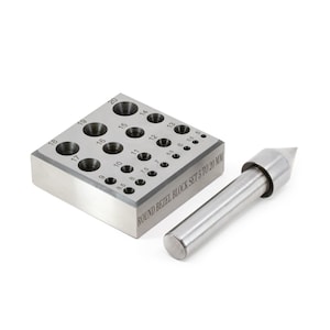 May include: A stainless steel round bezel block set with a matching punch. The block has multiple circular indentations, ranging from 5 mm to 20 mm, with corresponding size markings. The text "ROUND BEZEL BLOCK SET 5 TO 20 MM" is visible.