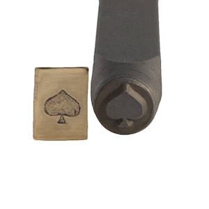 Puede incluir: Un sello de metal con un diseño de pica. El sello se utiliza para crear impresiones en metal.