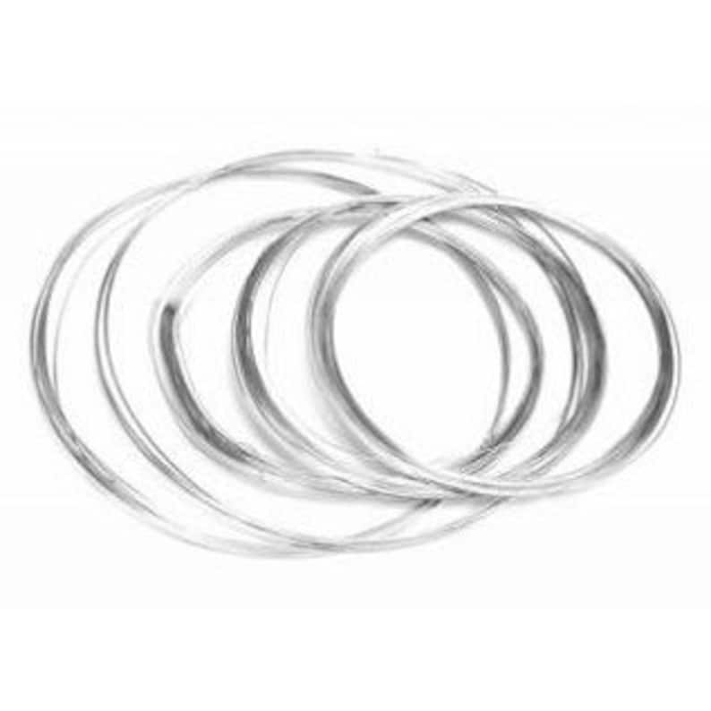 May include: A collection of thin, silver-colored metal bangles. The bangles are circular and appear to be made of a shiny, reflective material. They are arranged in a slightly overlapping pattern against a white background.