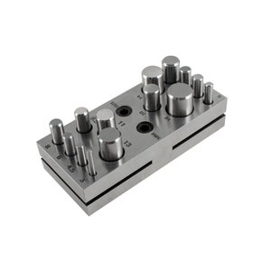 May include: A metal punch set with 14 different sized round punches. The punches are arranged in two rows on a metal base. The base is labeled with the sizes of the punches in millimeters.
