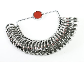 May include: A silver ring sizer with a red knob. The sizer has a series of rings numbered 1 to 13, and is used to determine the correct ring size.