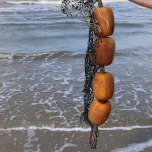 May include: A fishing net with four orange floats attached to a rope. The net is black and the floats are a weathered orange color. The background is a seascape with waves.