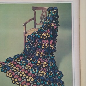May include: A crochet pattern for a pansy afghan, featuring a close-up of the finished product draped over a wooden chair. The afghan is made with a variety of colors, including blue, yellow, red, and green. The pattern includes instructions for creating the pansy motif, as well as the overall afghan.