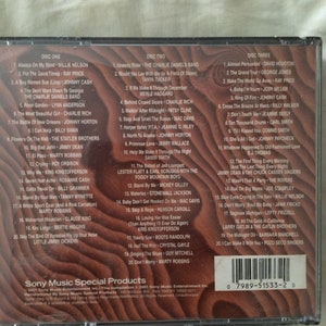 May include: A CD case with a black background and a white border. The front of the case features a title card with the text "Sony Music Special Products" and a barcode. The back of the case lists the songs on each of the three discs. The songs are listed by artist and title. The case is a compilation of country music hits.