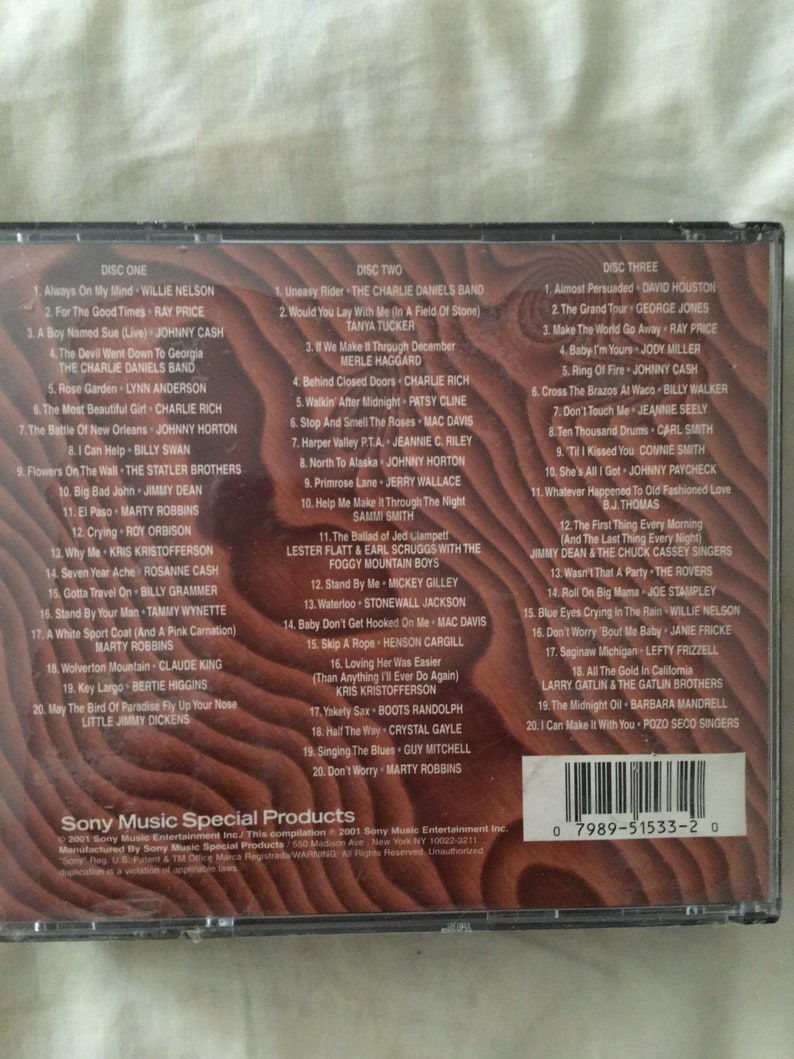 May include: A CD case with a black background and a white border. The front of the case features a title card with the text "Sony Music Special Products" and a barcode. The back of the case lists the songs on each of the three discs. The songs are listed by artist and title. The case is a compilation of country music hits.