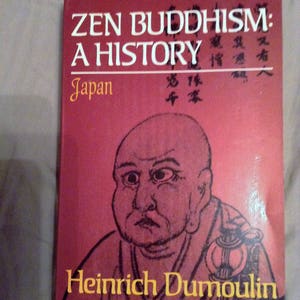 May include: A red book titled "Zen Buddhism: A History Japan" by Heinrich Dumoulin. The cover features a black and white illustration of a man with a shaved head.