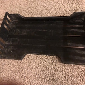 May include: A black plastic desk organizer with a rectangular shape. The organizer has a slatted design on the bottom and sides, with cut-out handles. It is designed to hold papers and documents.