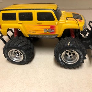 Può includere: Camion giocattolo Hummer H3 giallo telecomandato con grandi pneumatici neri. Il giocattolo ha molle di sospensione rosse e la scritta "NEW BRIGHT" sugli pneumatici. Il camion ha un paraurti anteriore nero e una ruota di scorta.