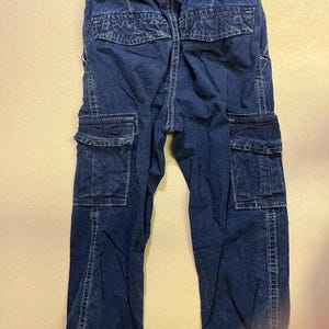 May include: Dark blue denim cargo pants with an elastic waistband and multiple pockets. The pants have a relaxed fit and are designed for comfort and durability. The stitching is visible in white.